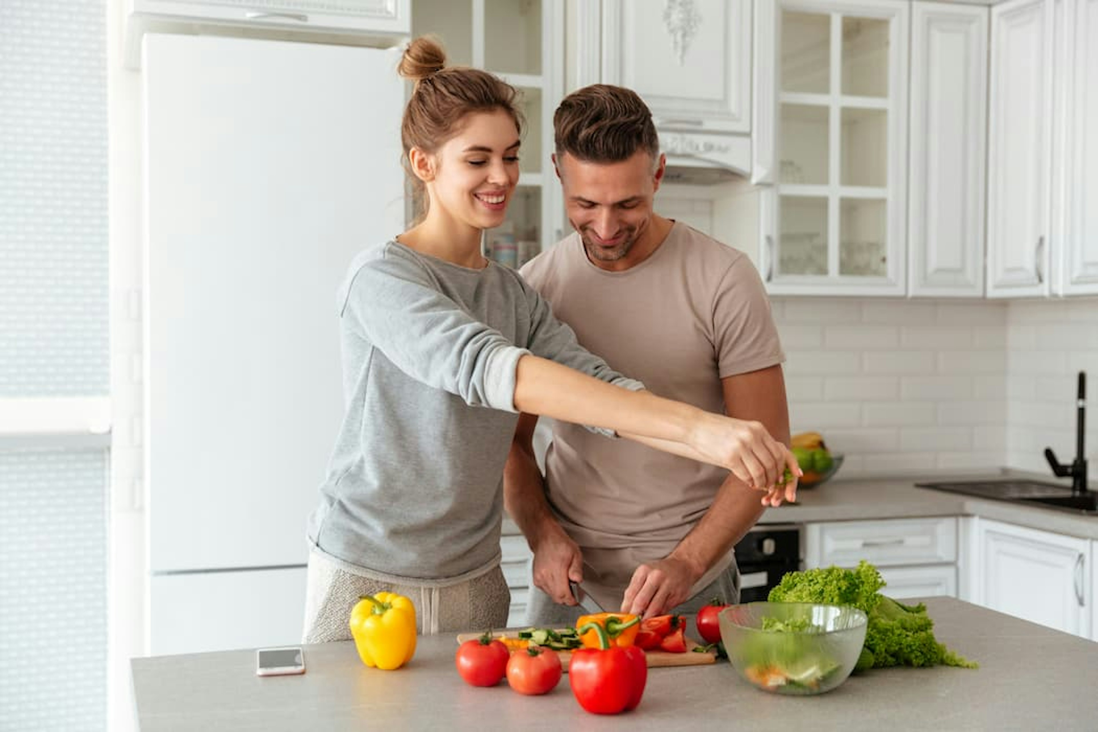 Um homem e uma mulher preparando uma salada em uma cozinha.